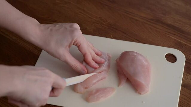 Woman cutting chicken breast on the table