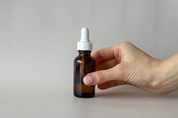 The Young Woman's hand holds a bottle with a dropper, with an oil or serum for facial and body care.