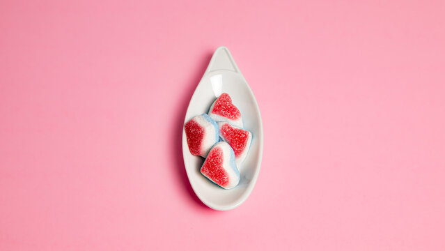 Gominolas de corazones sobre un plato pequeño blanco centrada, en fondo rosa 