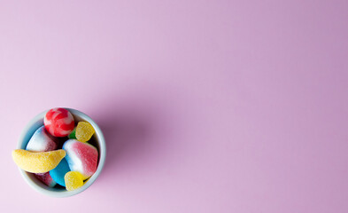 Fototapeta na wymiar Bol relleno de gominolas multicolores y caramelos sobre fondo rosa con espacio para texto