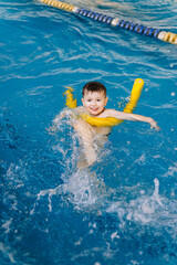 Happy little boy learning to swim with pool noodle