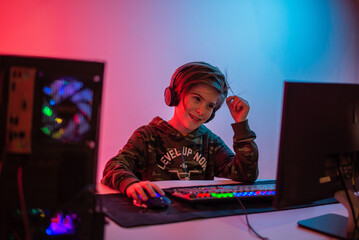 Portrait of  gamer boy playing video games on computer in dark room wearing headphones and using backlit colorful keyboard