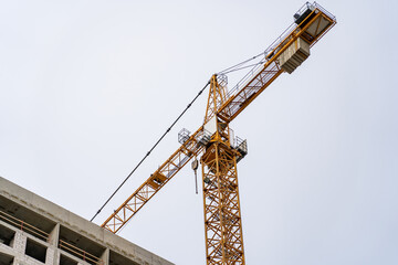 Yellow construction tower crane and unfinished residential building against grey sky