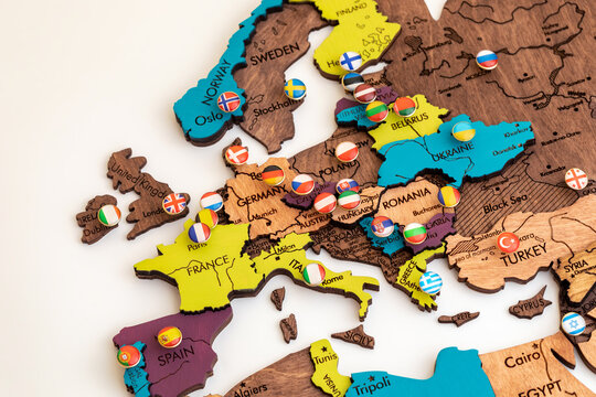 map of europe with flags, lots of round metal buttons with different flags of countries on the map of europe, wooden volume map of the world on a white background, politics, international