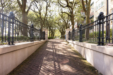 Ascending brick walkway into Charleston Riverfront Park, Charleston, South Carolina. Full sun and shadows, iron gates on either side of walkway. Trees leafed out. No people.