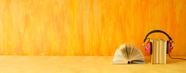audio book concept with row of books, one opened and vintage headphones,panoramic, yellow...