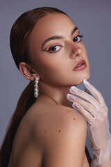 Young woman with red hair, brown eyes, clear skin, natural beauty, wearing white mesh glove and pearl earrings, looking to camera, with minimal makeup. Grey background. 