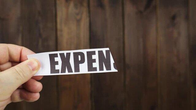 A man cuts with scissors a strip of paper with the inscription - EXPENSES.