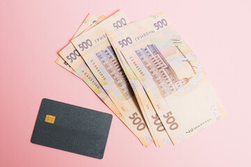 Flatlay, modern bank card with chip and Ukrainian hryvnia money on pink paper background