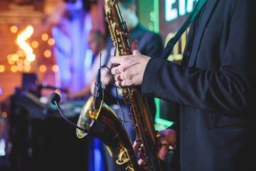 Obraz premium Concert view of saxophonist, a golden saxophone, sax player with vocalist and musical band during jazz orchestra show performing music on a stage in the scene lights