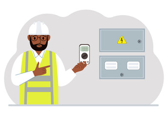 A male electrical engineer holds a digital multimeter in his hand and stands next to an electrical cabinet.