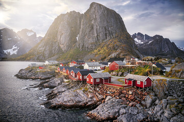 Typical red houses in Reine, Lofoten, Norway, overlooking the lake and the mountain during a clear spring day with clouds