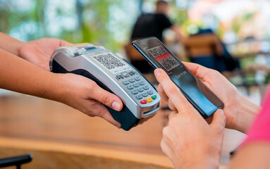 Woman using contactless payment by mobile phone with QR code at cafe