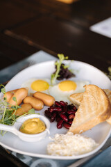 English breakfast. Fried eggs, red beans, mini sausages, butter, mustard and toasted bread