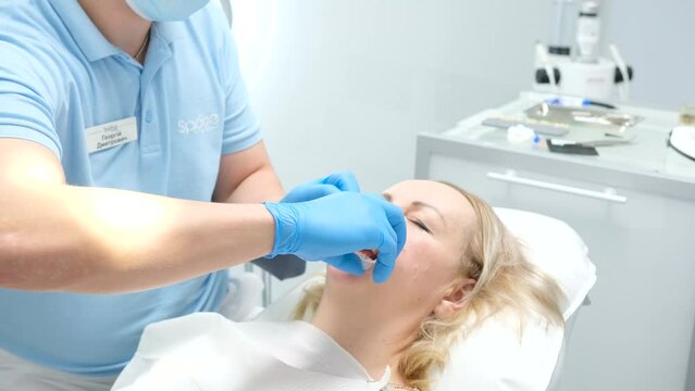 liquid cofferdam to isolate gums from action of bleaching agent optragat rotary spreader after end of dental procedure doctor removes mouth dilator takes glasses from protection photopolymer lamp