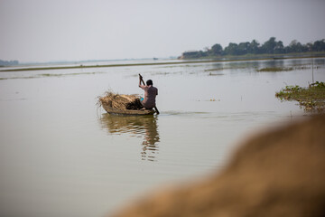 Selective focus on a man rowing a loaded boat to cross the river. Small boat with full of straws...