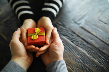 Top view of male and female hands holding gift box with ribbon on wooden background. Present for...