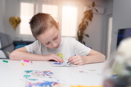 A boy of 4-7 years old sits at the table and draws with multi-colored paints. Children's creativity. Children's hobbies