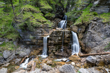 Wasserfall der sich teilt über Felsen im Wald mit grünen Bäumen und Moos. Kuhflucht Wasserfälle bei Farchant in Bayern. - obrazy, fototapety, plakaty