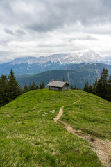Fototapeta na wymiar Hütte auf Almwiese in den Vergen mit Pfad oder Weg und Bergpanorama.