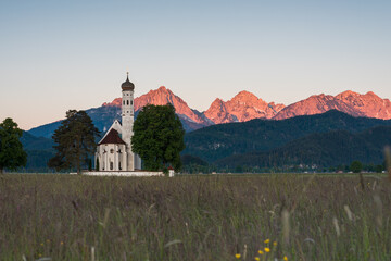 Kapelle auf Blumenwiese zum Sonnenaufgang im Alpenvorland im Allgäu.