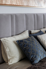Close-up of a new blue and gray bed with decorative pillows, fabric headboard in a bedroom in a staged model of a hotel or apartment. 
