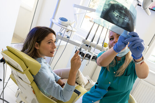 Dentist in the dental office talking with a female patient and preparing for treatment. Examining the x-ray image.	
