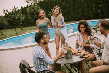 Group of young people cheering with cider by the pool in the garden