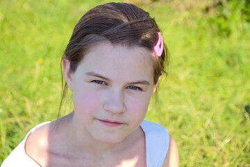 Close-up portrait of a girl. The girl sits on the green grass in the park and looks at the camera.
