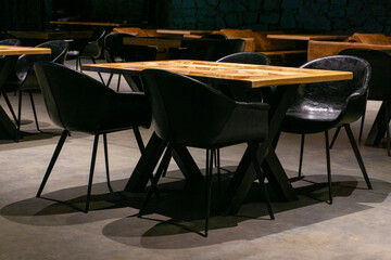 Empty semi-dark restaurant hall with black leather chairs and wooden tables