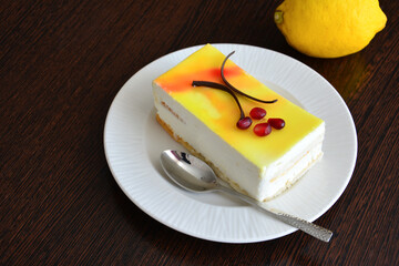 A piece of lemon cake with a spoon on a plate with a lemon on background 