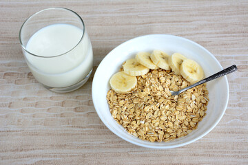 A bowl of oatmeal with banana slices, teaspoon and a glass of milk isolated, close-up