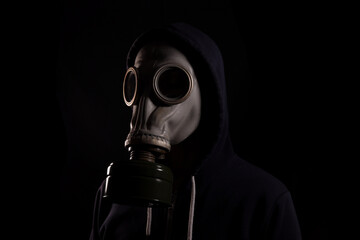 Man in a hood in a gas mask on a black background, the concept of environmental pollution,...