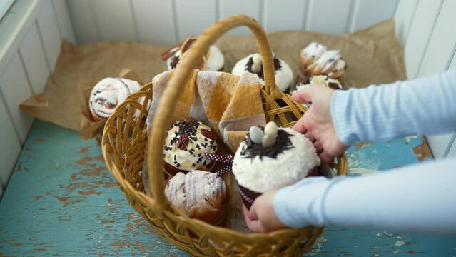 Female hands put Easter cakes creatively decorated with white icing, candied fruits, nuts and chocolate into authentic plaited basket. Stylish traditional Easter buns.