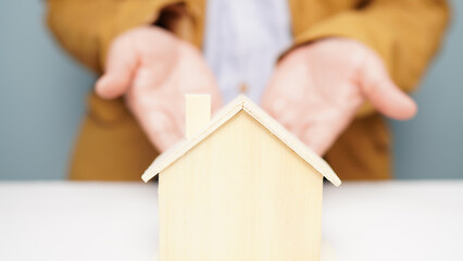 Model of a wooden house with a man showing his hands behind the scenes Businessman and real estate concept