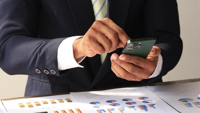 Business man looking at financial information from a mobile phone, he is checking company financial documents, he is an executive of a startup company. Concept of financial management.