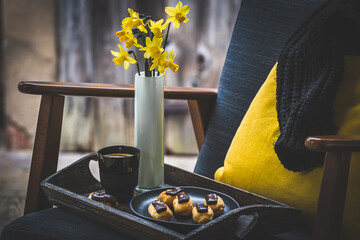 Wooden tray with mini eclairs, coffee and flowers on a wooden tray on an armchair in front of the...