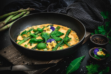 Omelette with green asparagus, basil and herbs on black background