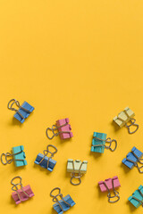 Many colorful binder clips on a yellow background. Copy space. Top view.