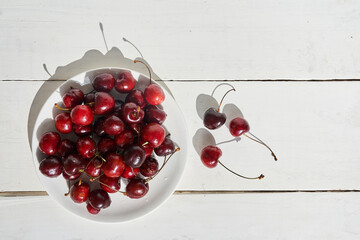 A plate of ripe red cherries on a white wooden background. With space to copy. A close-up view of a plate of cherries from above. High quality photo