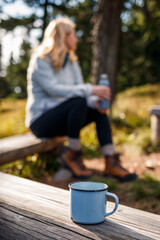 Travel mug on wooden bench. Relaxation during hiking outdoors. Woman camping in forest