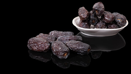 Medjoul dates, on a white bowl on a black background.