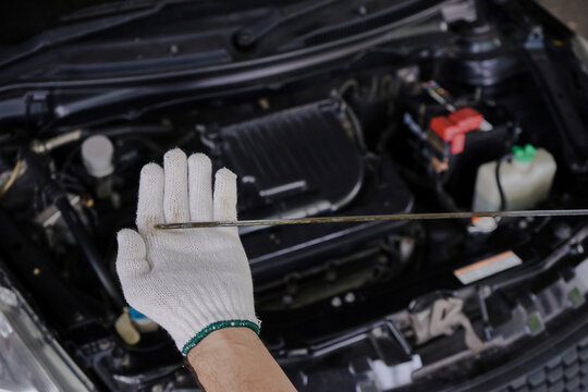 A gloved mechanic's hand is holding an oil dipstick to check the engine oil level. - Powered by Adobe