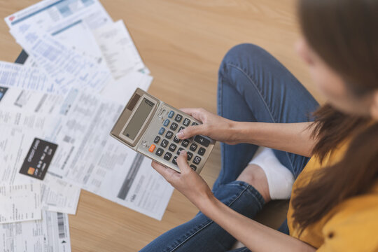 Stress, owe asian young employee woman hand press on calculator to calculate budget, cost income, expenses of credit card on statement for payment, sitting on floor at home. Financial, finance people.