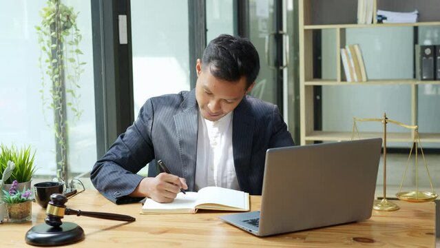 Portrait of Asian man lawyer studying case for client before going to court using computer and notebook to work