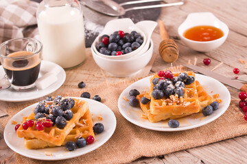 Waffles with red currant and blueberries on white dish.