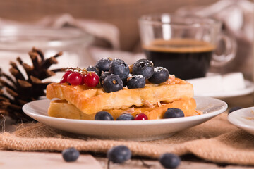 Waffles with red currant and blueberries on white dish.