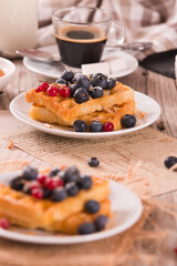 Waffles with red currant and blueberries on white dish.