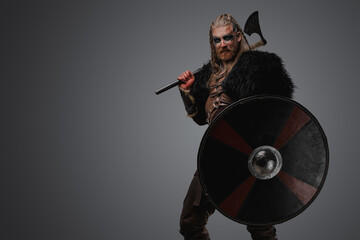 Fototapeta na wymiar Studio shot of isolated on gray background viking with black fur holding shield and axe.