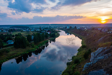sunset over the river and valley with a settlement on a background of pink clouds, smooth water surface with a reflection of sky